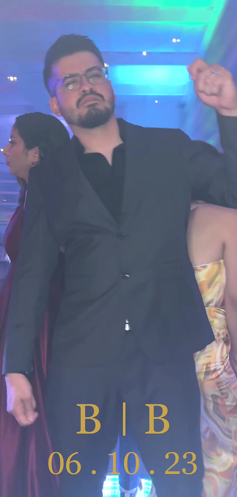Man in a dark suit dancing at a party under colored lights