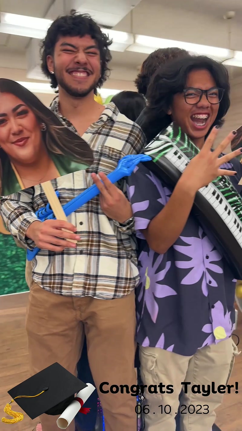 Two guests posing with a face cutout prop and a keyboard prop at a graduation party