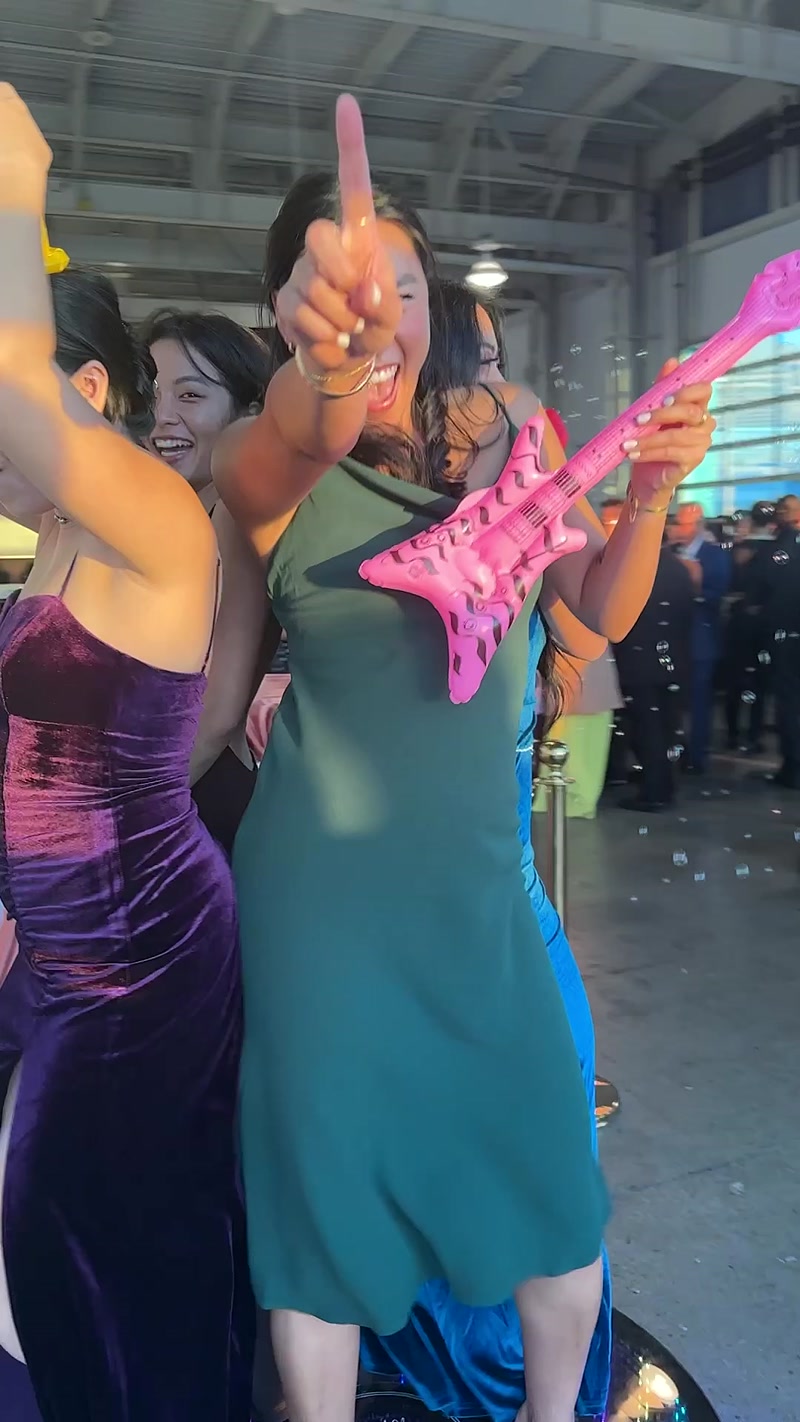 Woman in a green dress pointing up while holding a pink inflatable guitar at a party